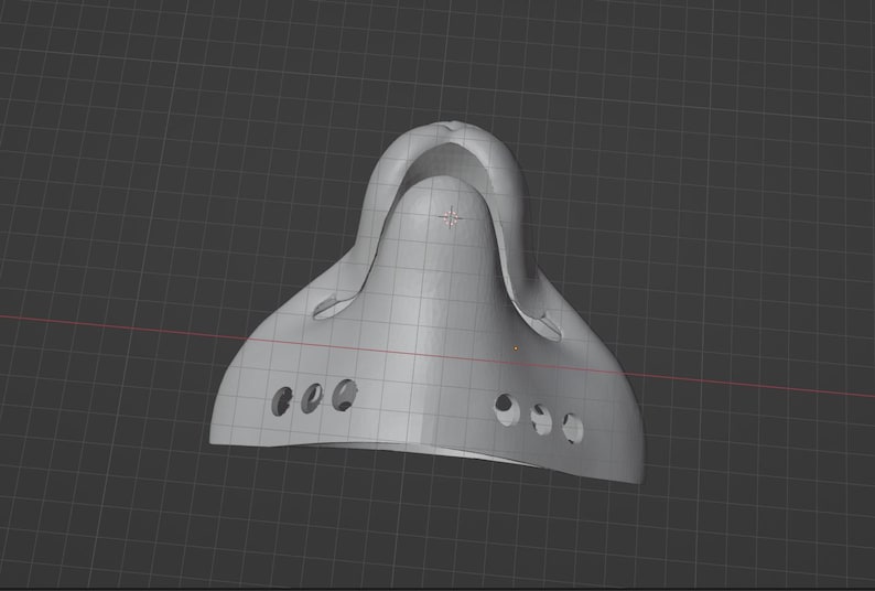 May include: A light gray, 3D-rendered object with a curved, helmet-like shape. It features a series of small, circular holes along the bottom edge and a raised, arched section at the top. The object is set against a dark gray grid background.