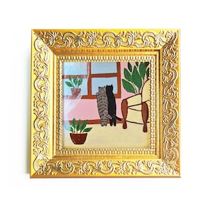 Puede incluir: Un cuadro cuadrado en un marco dorado ornamentado que representa a dos gatos, uno atigrado y otro negro, de pie uno al lado del otro mirando por una ventana. La escena incluye una pared rosa, una silla marrón y dos plantas verdes en macetas.