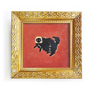 Puede incluir: Pintura enmarcada que presenta un gato negro con detalles blancos sobre un fondo rojo. El gato está representado en una pose juguetona. El marco dorado tiene detalles ornamentales.