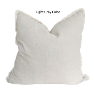 May include: A light gray throw pillow with a white fringe border. The pillow is made of a soft, textured fabric.
