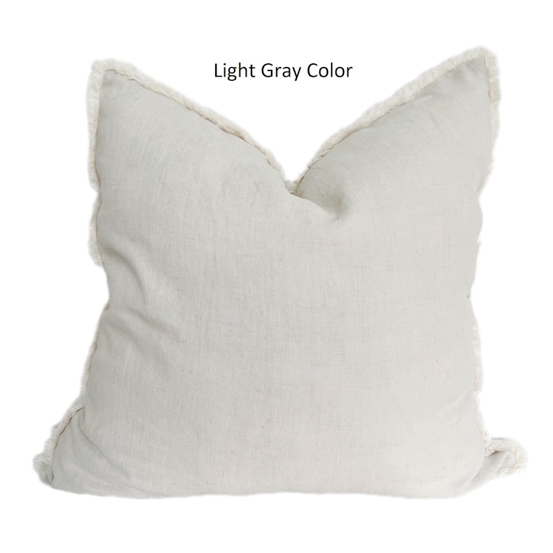 May include: A light gray throw pillow with a white fringe border. The pillow is made of a soft, textured fabric.