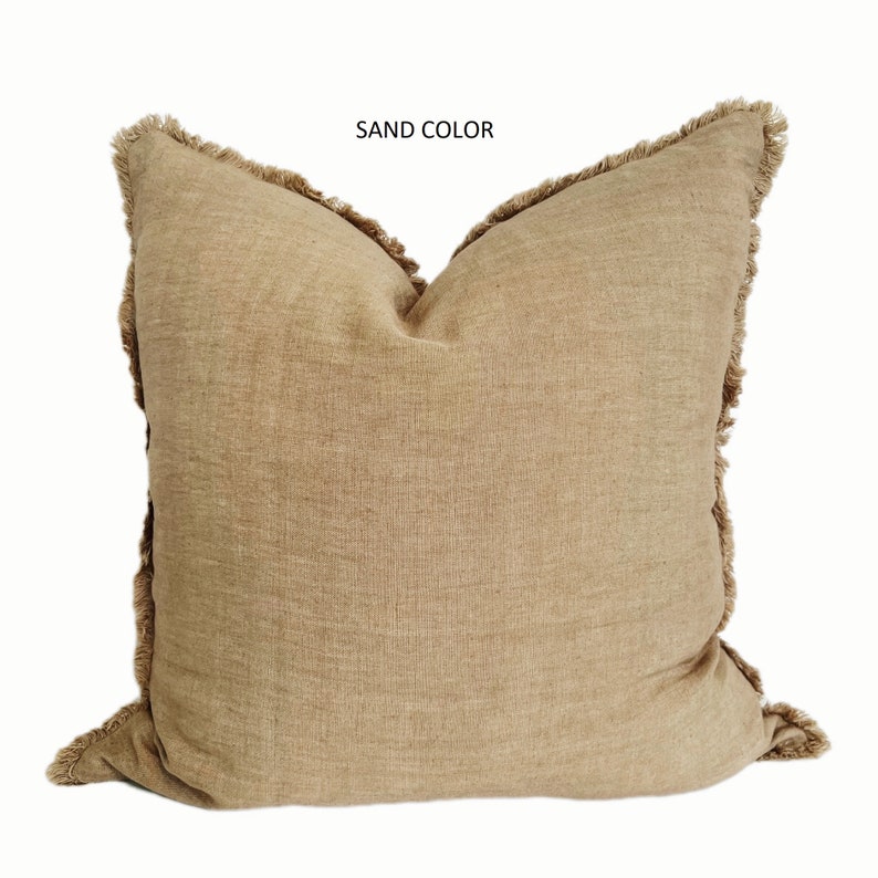 May include: A sand-colored throw pillow with a fringed border. The pillow is made of a soft, textured fabric.