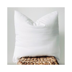May include: A white pillow with a smooth, textured surface. The pillow is sitting on a woven wicker basket.