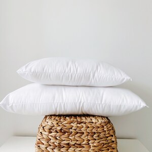 May include: Two white pillows stacked on top of each other, resting on a woven wicker basket.