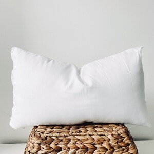 May include: A white pillow resting on a woven wicker basket.