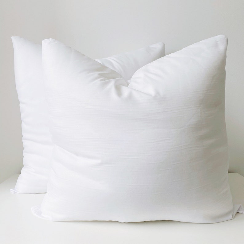 May include: Two white pillowcases, made of a soft, smooth fabric. The pillowcases are lying flat on a white surface.