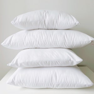 May include: Four white pillows stacked on top of each other. The pillows are all made of a soft, white fabric and have a smooth, even surface.