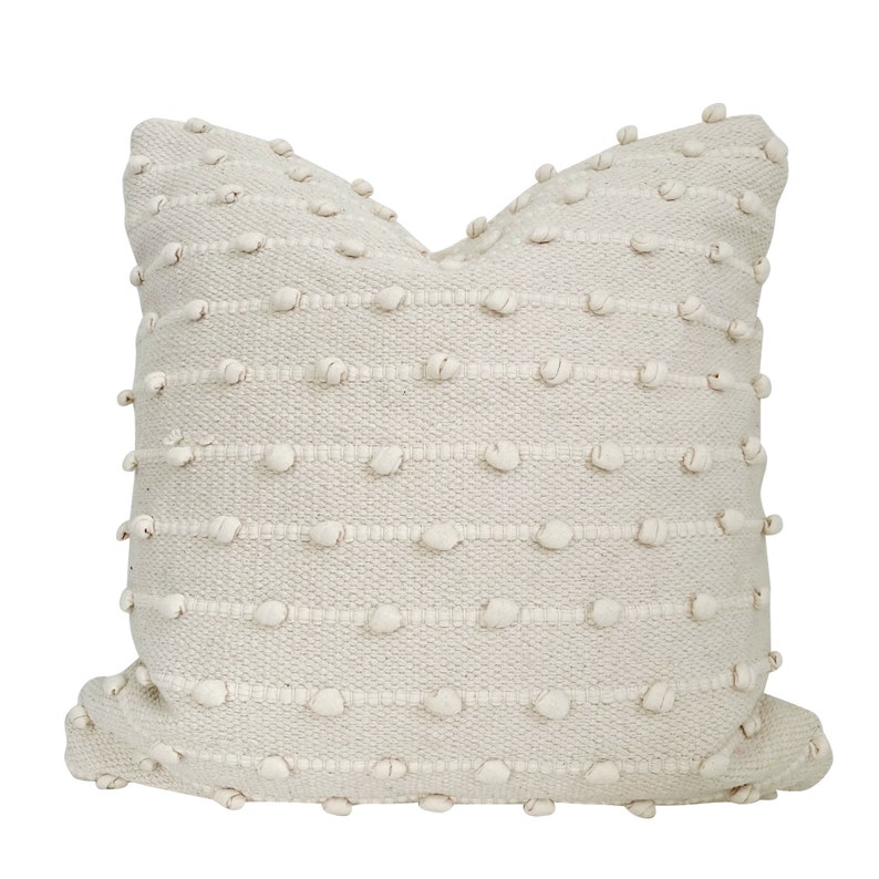 May include: A cream coloured throw pillow with a textured woven design featuring small raised bumps.