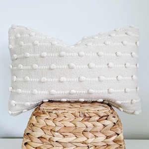 May include: A white throw pillow with a textured, raised dot pattern. The pillow is sitting on a woven wicker basket.