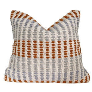 May include: A decorative throw pillow with a geometric pattern of orange and gray stripes and dots. The pillow is made of a soft, textured fabric.