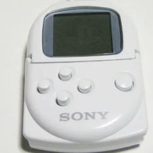 Può includere: Un dispositivo di gioco portatile bianco con un piccolo schermo e diversi pulsanti. Il dispositivo presenta il marchio "SONY" sulla parte anteriore. Lo schermo è scuro e i pulsanti sono circolari.
