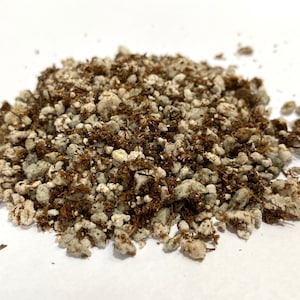 May include: A close-up of a pile of brown and white potting mix. The mix is made up of small, irregular pieces of bark and white pebbles.