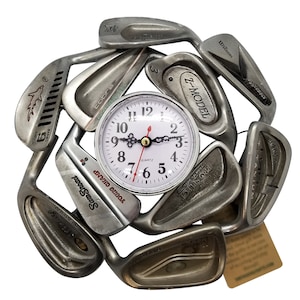 May include: A clock made from golf clubs with a white face and black numbers. The clock is surrounded by golf clubs with various brand names, including Wilson, Cobra, and Sam Snead.