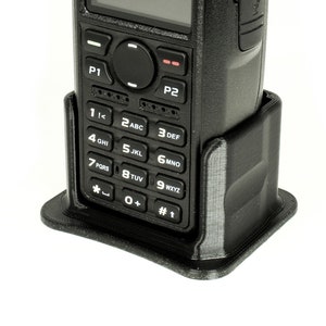 May include: A black AnyTone two-way radio with a keypad and a screen. The radio is in a black charging cradle.