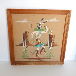 May include: A vintage wall clock with a wooden frame. The clock face features a Native American figure in traditional attire, with a desert landscape backdrop. The clock hands are gold-colored.