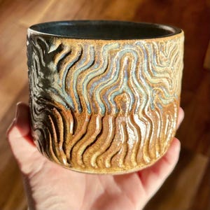 May include: A white ceramic mug with a black handle and the text "But First, Coffee" in a black, bold font. The mug is on a white surface.