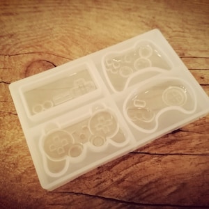 Puede incluir: Un molde de silicona blanco con cuatro diseños diferentes de mandos de videojuegos. El molde está diseñado para crear manualidades de resina.