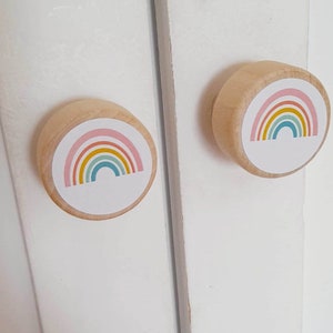 May include: Two wooden cabinet knobs featuring a rainbow design. The knobs are round and have a white background with a multi-coloured rainbow.
