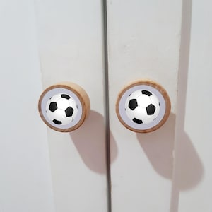 May include: Two wooden cabinet knobs with a white background and a black and white soccer ball design.