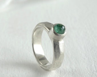 May include: A silver ring with a hammered texture and a green gemstone set in the center.