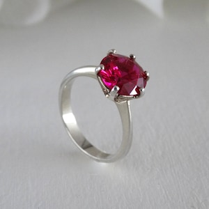 Op de afbeelding: Een zilveren ring met een grote, ovale, felroze edelsteen.