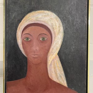 Puede incluir: Retrato de pintura al óleo de una persona con un tocado blanco y ojos verdes. La piel de la persona es de color marrón rojizo y el fondo es oscuro. La pintura está enmarcada en un marco dorado.