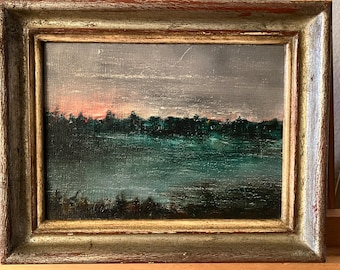 Op de afbeelding: Een ingelijst olieverfschilderij dat een landschapsscene voorstelt met een meer op de voorgrond en een rij bomen op de achtergrond. De lucht is een gedempte paars met een vleugje roze in de verte.