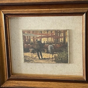 Pode incluir: Uma pintura a aquarela emoldurada que retrata uma cena movimentada de mercado ao ar livre. A pintura apresenta um grupo de pessoas reunidas sob um toldo vermelho, com um homem de casaco escuro em destaque em primeiro plano. A assinatura do artista, "J. Barrett", é visível no canto inferior esquerdo.