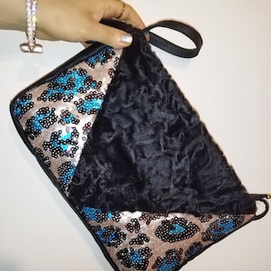 Puede incluir: Un clutch negro con un diseño único. Una sección presenta un material negro texturizado, mientras que la otra muestra un estampado de leopardo con lentejuelas en plata, negro y turquesa. El clutch tiene un asa negra.