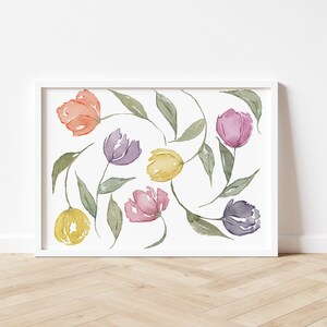 Peut inclure: Peinture à l'aquarelle de tulipes colorées dans des tons orange, violet, rose et jaune, avec des feuilles et des tiges vertes. L'œuvre est encadrée dans un cadre rectangulaire blanc, sur un mur blanc et un sol en bois.