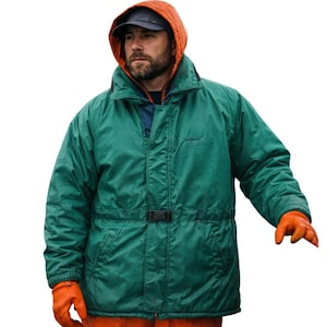 May include: A teal green hooded jacket with a black buckle belt, worn over an orange hooded sweatshirt and a navy blue baseball cap. The person is wearing orange gloves. The jacket has a high collar.