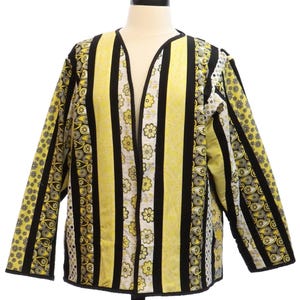May include: A long-sleeve open-front jacket featuring vertical panels of yellow and black fabric. The design includes alternating stripes of floral patterns, paisley prints, and solid black bands, creating a quilted appearance throughout the garment.