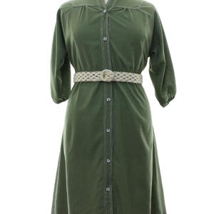 May include: An olive green button-down dress featuring a mandarin collar, three-quarter length sleeves with gathered cuffs, and white contrast stitching along the front placket and shoulders, cinched with a woven beige belt.