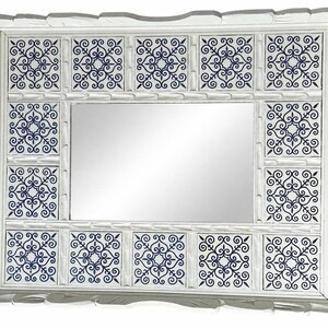 May include: A rectangular wall mirror featuring a white wooden frame with a scalloped edge. The frame is decorated with twelve square tiles, each displaying a dark blue intricate filigree pattern on a white background surrounding the central glass.