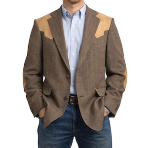 May include: A brown tweed blazer with tan suede patches on the shoulders and elbows. The blazer has a two-button closure, two front pockets, and a notched lapel. The person is wearing a light blue button-down shirt and blue jeans.