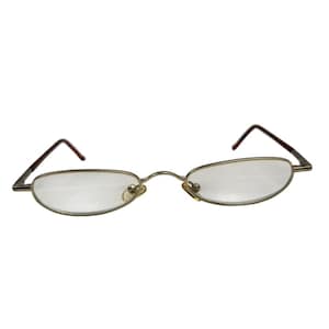 May include: A pair of oval-shaped reading glasses with a thin, metallic gold-toned frame. The glasses feature clear lenses, a curved bridge, and dark brown temple tips. The design is narrow and lightweight, with adjustable nose pads visible.