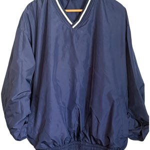 Op de afbeelding: Een marineblauw windjack met lange mouwen en een V-hals met witte bies. Het kledingstuk heeft een elastische tailleband en een label aan de binnenkant van de halslijn met de tekst "JOE'S SPORTS GEAR" in witte en rode letters.