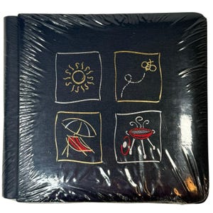 Puede incluir: Un álbum de fotos azul oscuro envuelto en plástico. La portada presenta cuatro cuadrados bordados con diseños de temática veraniega: un sol, una abeja, una silla de playa con sombrilla y una barbacoa.