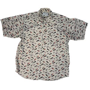 Op de afbeelding: Een overhemd met korte mouwen en knoopsluiting in een lichtbeige kleur, voorzien van een all-over print van diverse vislokaas in zwart, rood en wit. Het overhemd heeft een kraag, een knoopsluiting aan de voorzijde en een klein Columbia-label.