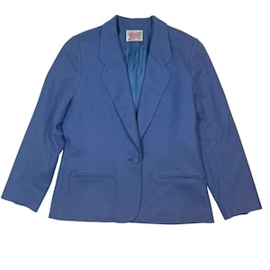 May include: A periwinkle blue blazer featuring a single-button closure, notched lapels, and two front welt pockets. The interior is lined with a matching blue fabric and includes a white rectangular brand label at the center of the neckline.