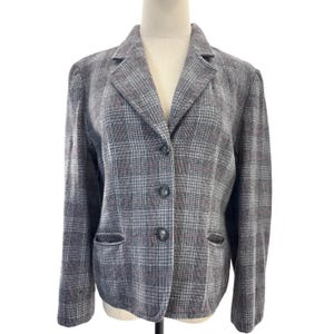 May include: A gray and black plaid blazer featuring a notched lapel, long sleeves, and a three-button front closure. The garment includes two front welt pockets and is displayed on a mannequin, showcasing a structured fit with a classic pattern.