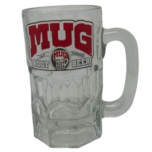 May include: Clear glass mug with a handle, featuring the word "MUG" in red block letters. Below the word "MUG" are the words "OLD ROOT" and "FASHIONED BEER". The mug has a textured, faceted design.
