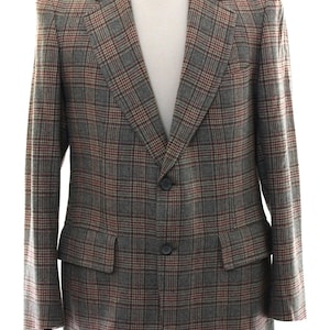 Peut inclure: Un blazer avec un motif à carreaux gris, marron et rouille. Le vêtement présente des revers crantés, deux boutons foncés pour la fermeture et deux poches à rabat sur le devant. La veste à manches longues est présentée sur un mannequin.