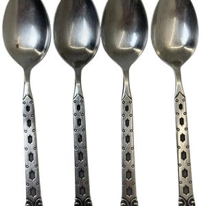 May include: A set of four silver-toned metal spoons arranged vertically. Each spoon features a smooth, oval-shaped bowl and a straight handle decorated with a repeating geometric pattern of small circles and elongated hexagons, ending in a scroll design.