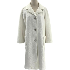 May include: A long, off-white coat with a textured, geometric pattern. The coat features a notched collar, three decorative buttons, and two front pockets. The coat is displayed on a mannequin.