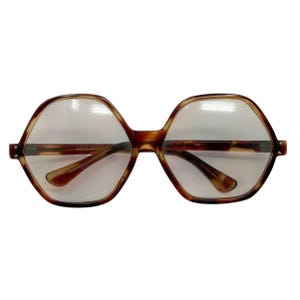 Peut inclure: Lunettes marron à motif écaille de tortue avec de grandes montures hexagonales. Les lunettes ont un design classique et vintage avec un pont et des branches visibles. Les verres sont clairs, et le style général est rétro.