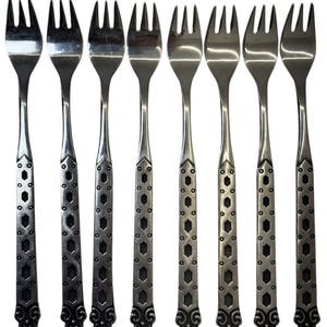 Puede incluir: Un juego de ocho tenedores de cóctel de metal plateado dispuestos en fila. Cada tenedor tiene tres dientes y un mango decorado con un patrón geométrico repetitivo de hexágonos y puntos, terminado con un diseño de volutas decorativo en la base.