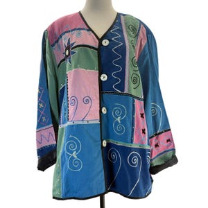 Puede incluir: Una chaqueta de manga larga con botones y diseño de patchwork en tonos azul, verde y rosa. La prenda está decorada con varios patrones bordados que incluyen espirales, zigzags y una estrella, terminada con cuatro botones blancos grandes.