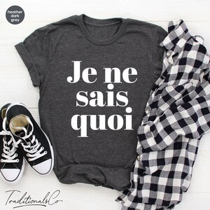 May include: A dark heather grey t-shirt with the French phrase "Je ne sais quoi" printed in white.