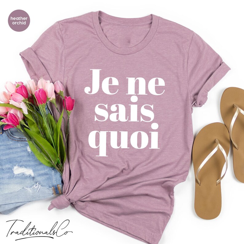 May include: A heather orchid colored t-shirt with the French phrase "Je ne sais quoi" printed in white on the front.